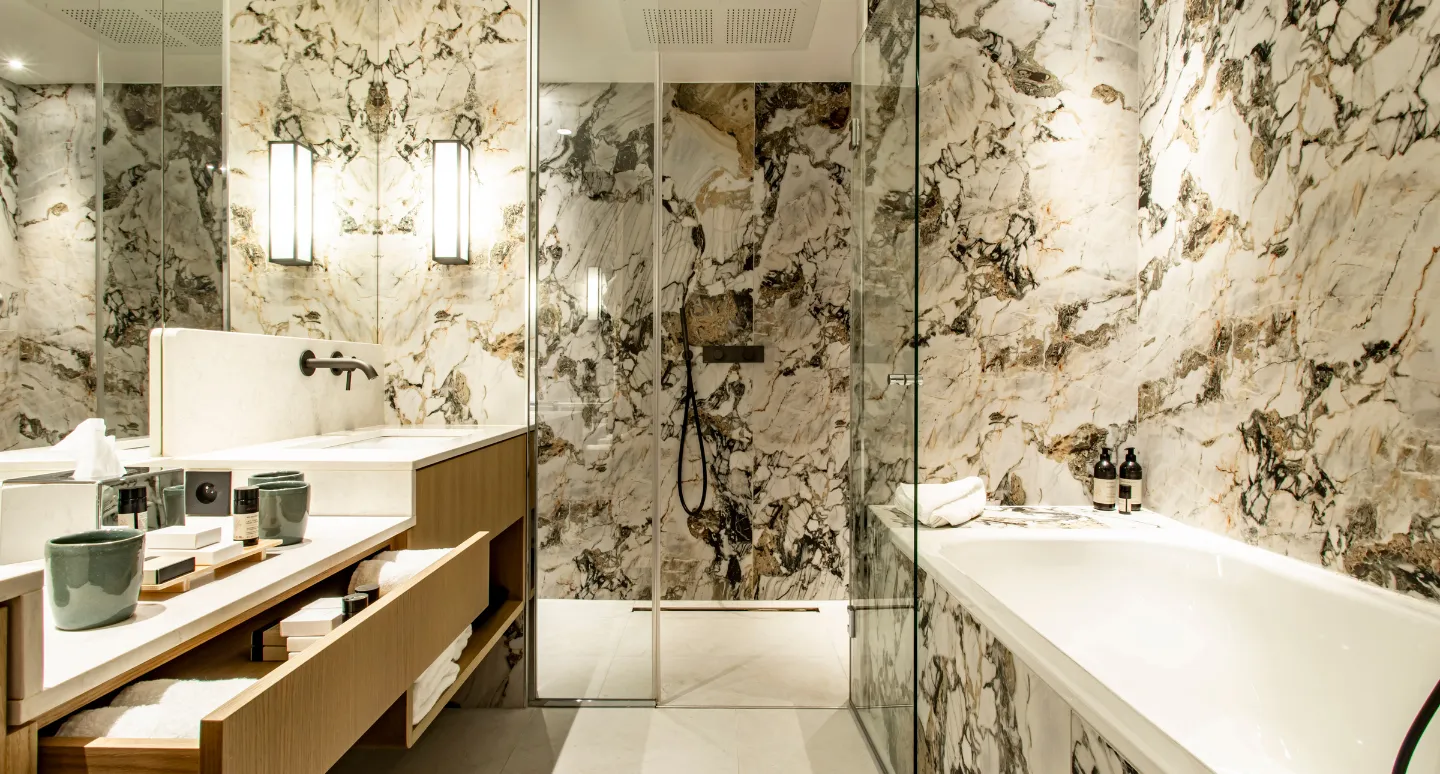 Salle de bain habillée de marbre veiné doré et noir, avec double vasque en bois, douche vitrée et baignoire