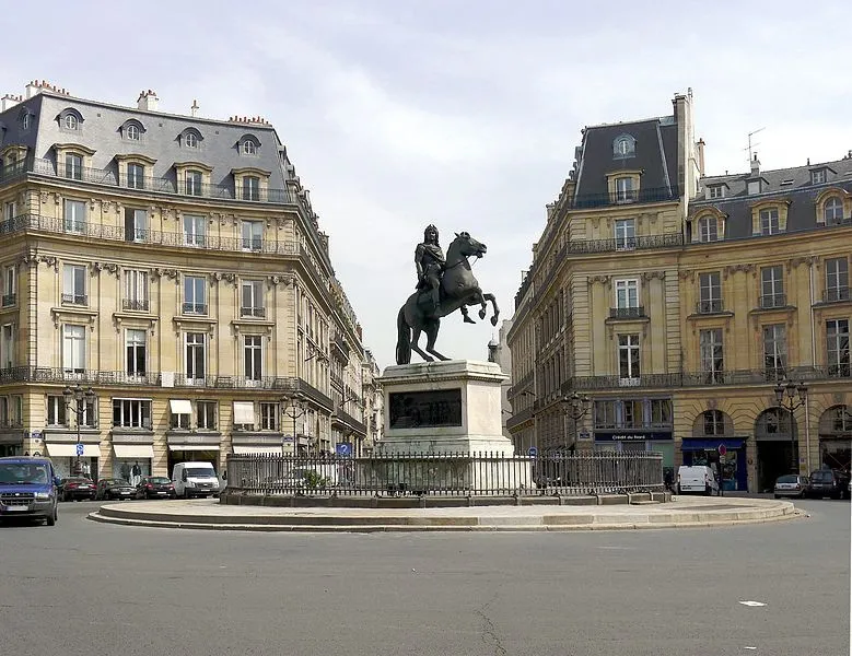 Vue d'ensemble d'une place parisienne avec statue équestre entourée de grilles, encadrée d'immeubles haussmanniens symétriques