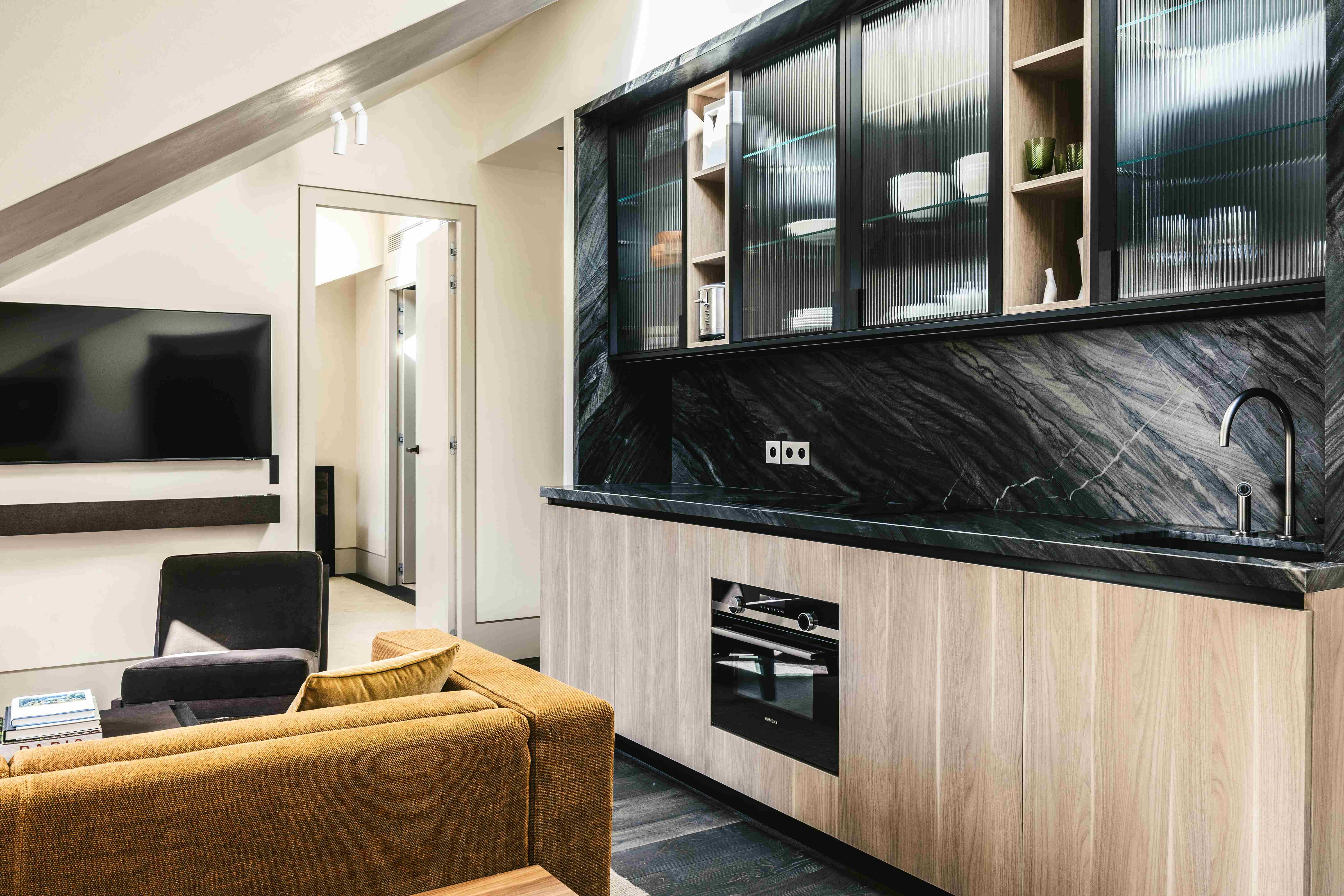 Suite mansardée avec kitchenette en marbre noir et bois, canapé moutarde et télévision murale