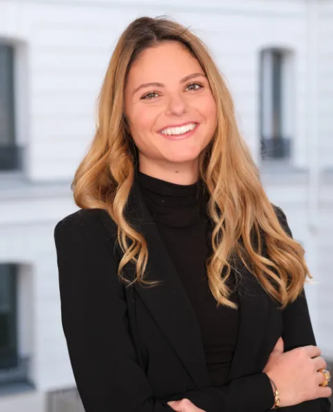 Portrait souriant d'une femme aux cheveux blonds ondulés, en tenue noire, devant une façade parisienne