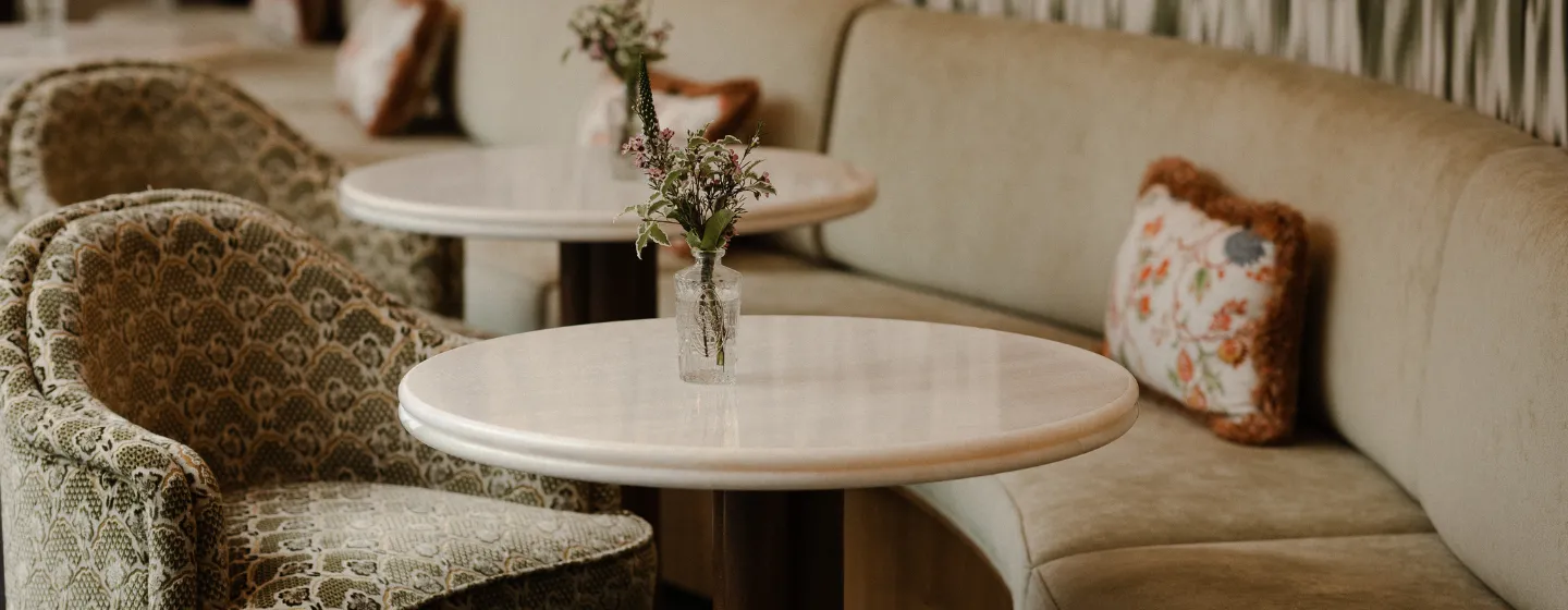 Salon avec fauteuils à motifs, tables rondes en marbre décorées de bouquets de fleurs et banquette avec coussins brodés
