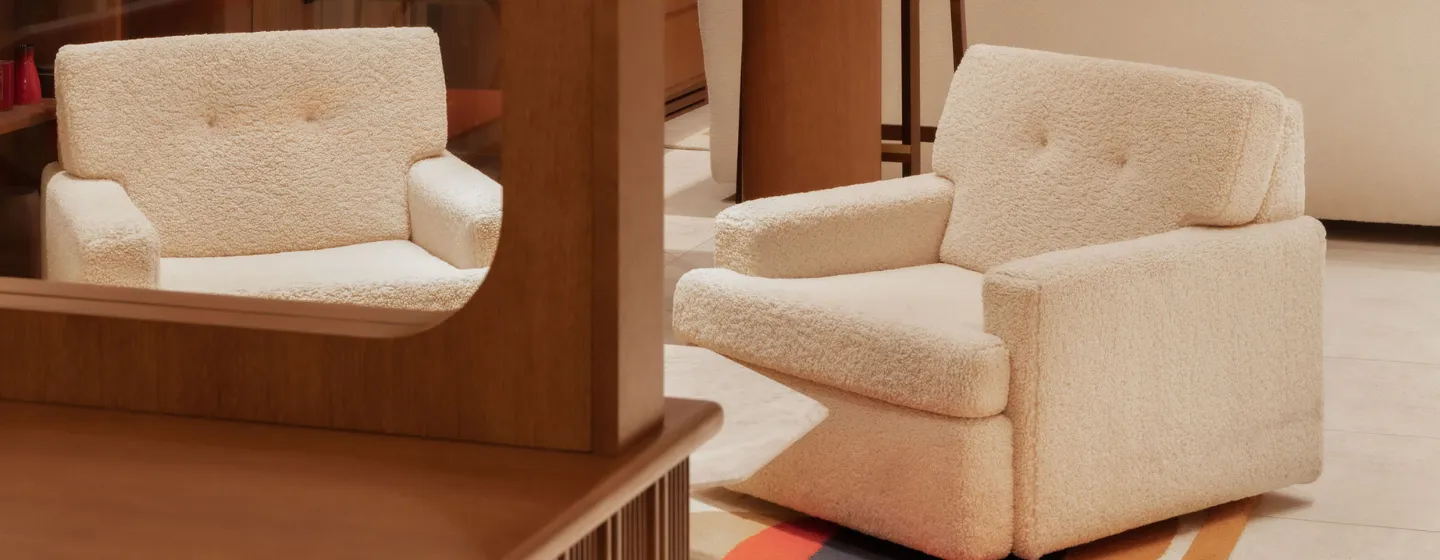 Fauteuil en bouclette blanche reflété dans un miroir, dans un salon aux tons chauds avec tapis coloré