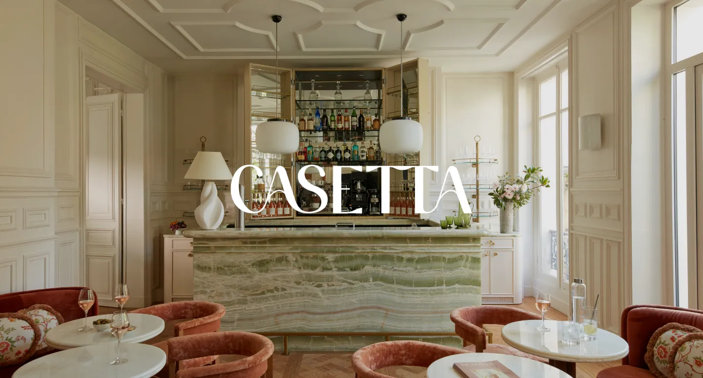 Bar Casetta en marbre vert veiné avec fauteuils orange en velours, logo blanc superposé sur boiseries claires
