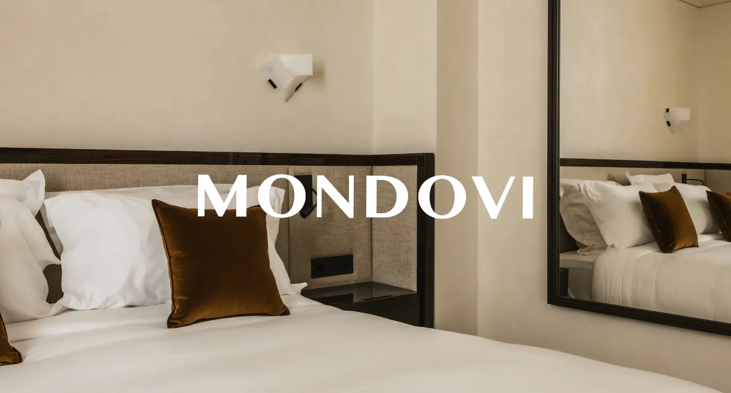 Chambre d'hôtel Mondovi avec lit blanc et coussin en velours brun, texte du logo superposé sur la photo