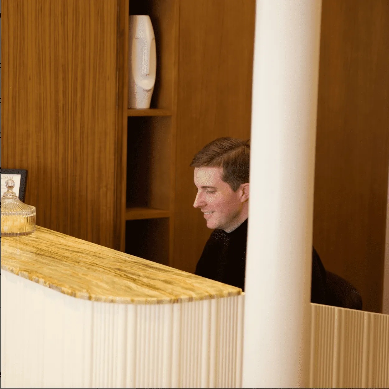 Réceptionniste souriant derrière un comptoir en marbre doré, dans un décor en bois chaleureux