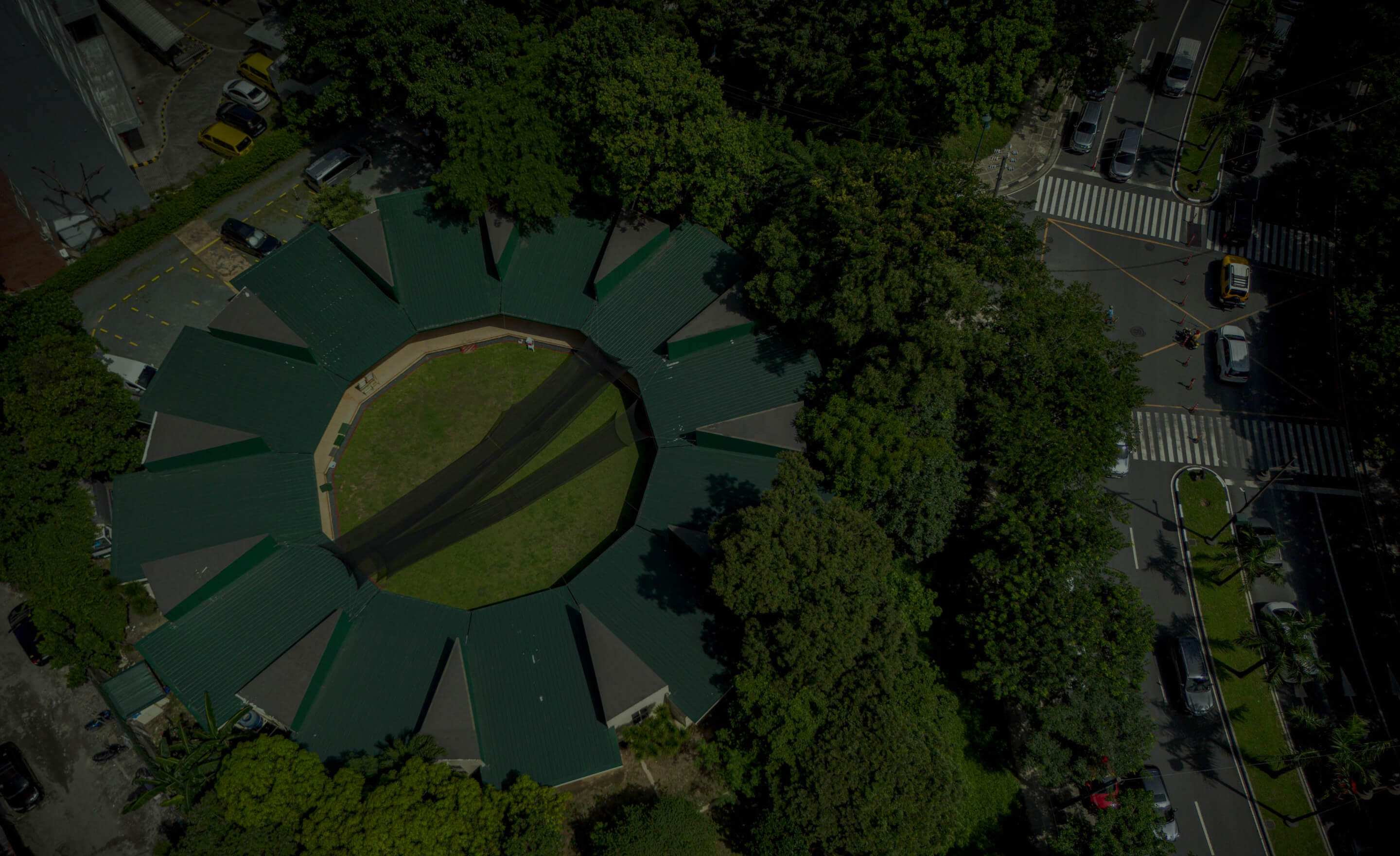 Aerial view of a circular green-roofed building with a grass courtyard surrounded by trees.