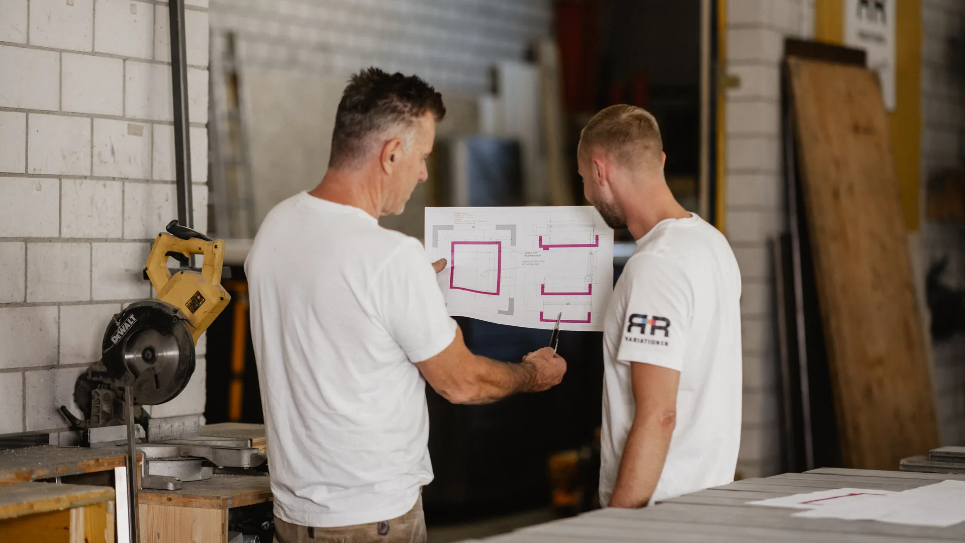 Zwei Mitarbeiter besprechen Bauplan in der Werkstatt, Planung individueller Wellnessanlagen von RR Variationen