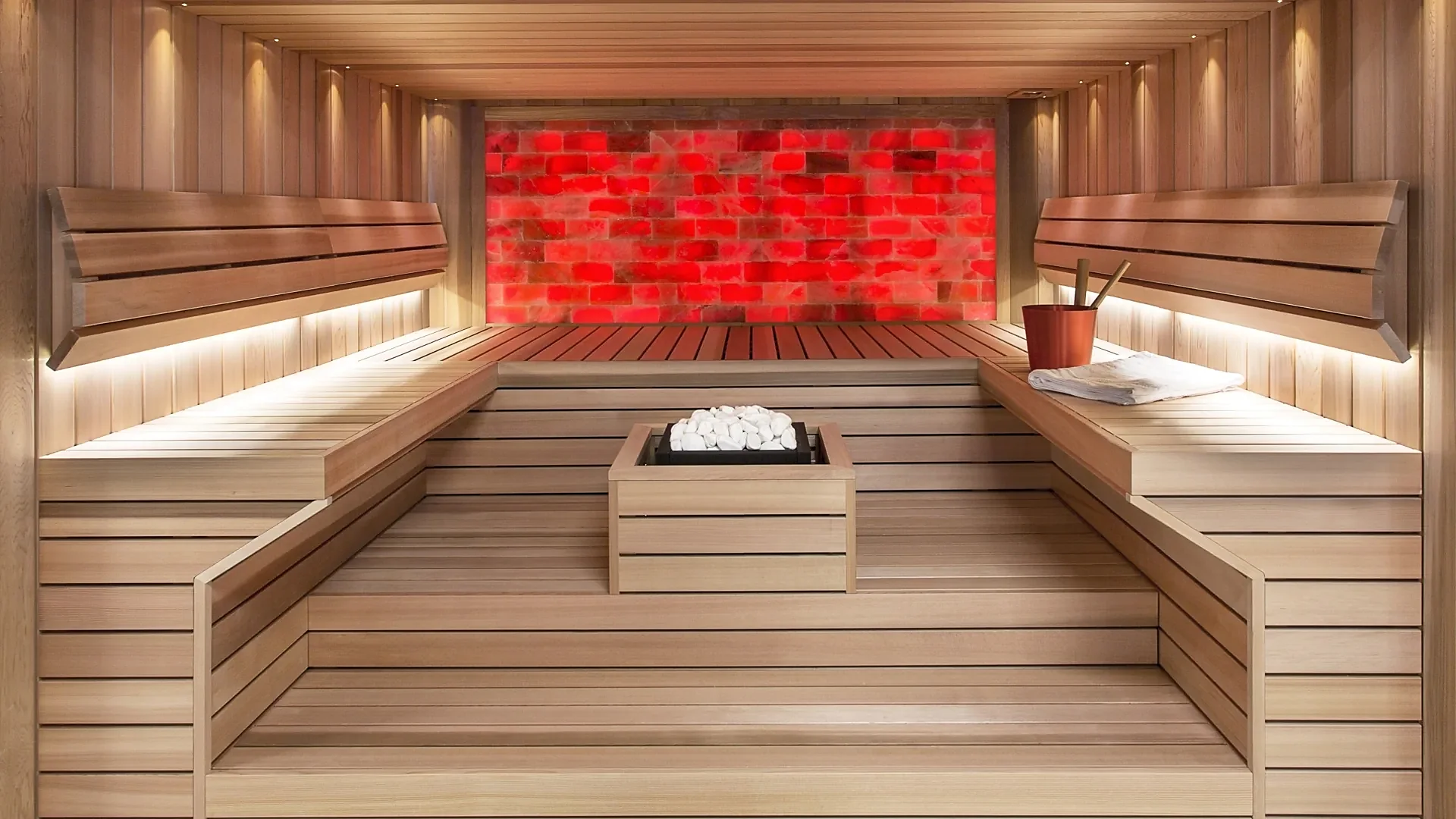 Sauna mit Salzsteinwand, beleuchteten Liegen und Ofen in der Mitte, Sauna nach Mass von RR Variationen