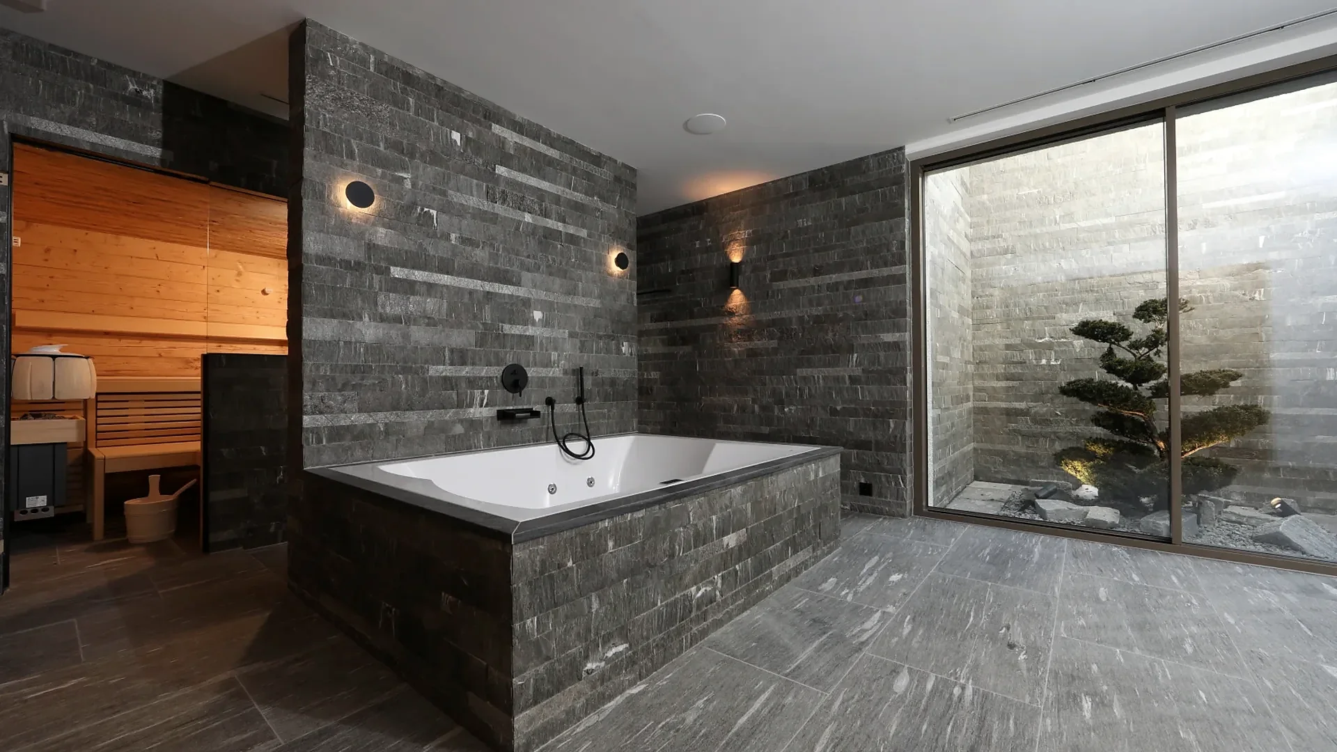 Wellnessbereich mit Natursteinwänden, Whirlwanne und Holzsauna im Hintergrund, klassische Sauna von RR Variationen