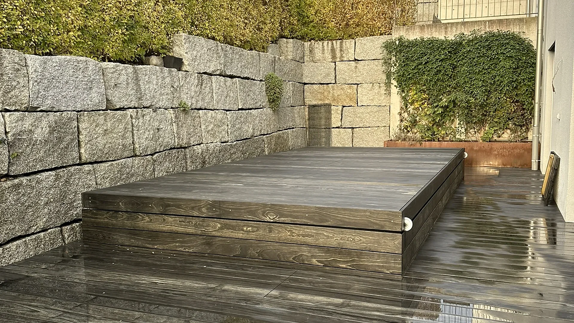 Geschlossene Holzabdeckung als Terrassenfläche vor Granitmauer, Swim Spa mit Abdeckung von RR Variationen