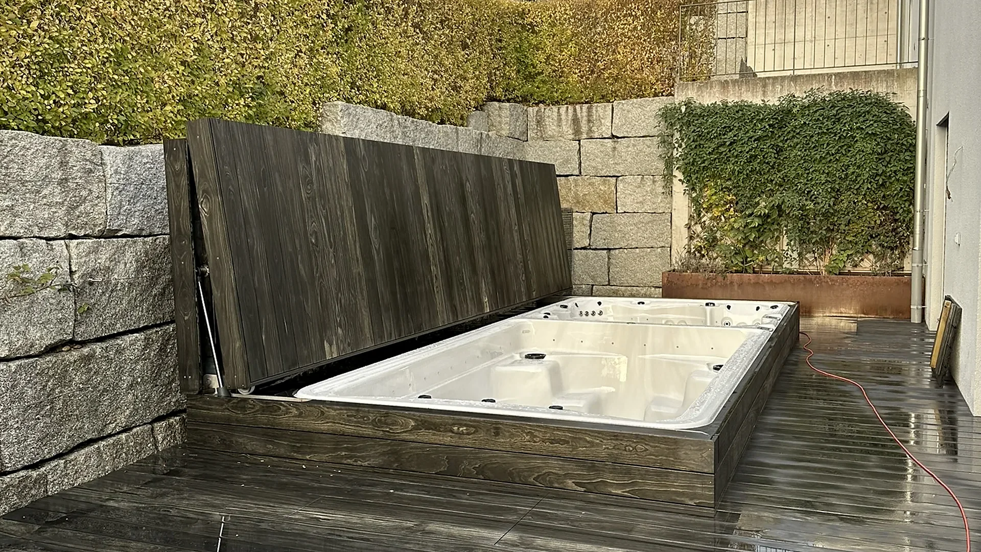 Swim Spa mit hochgeklappter Holzabdeckung vor Granitmauer auf Terrasse, Swim Spa von RR Variationen