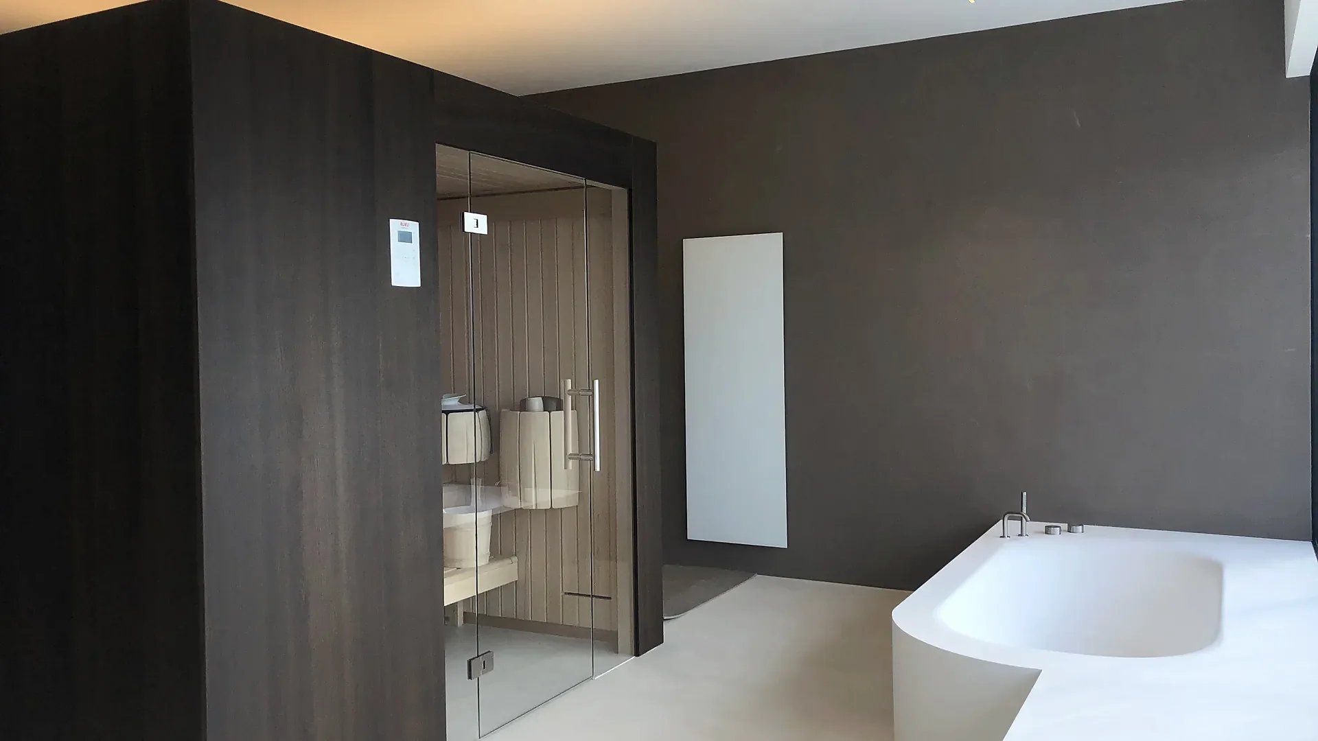 Saunakabine in dunklem Holz mit Glastür neben freistehender Badewanne, RUKU Thermium von RR Variationen