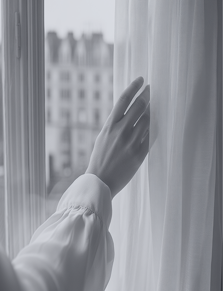 Woman standing by a window, hand touching a sheer curtain