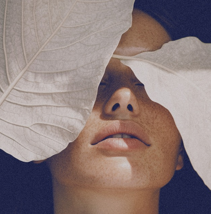 Close-up portrait of woman with leaf covering her eyes