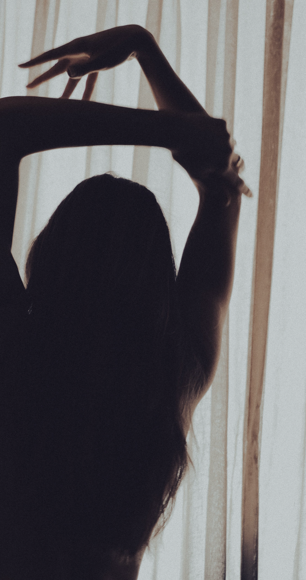 Woman with arms raised, hair covering face, dramatic lighting