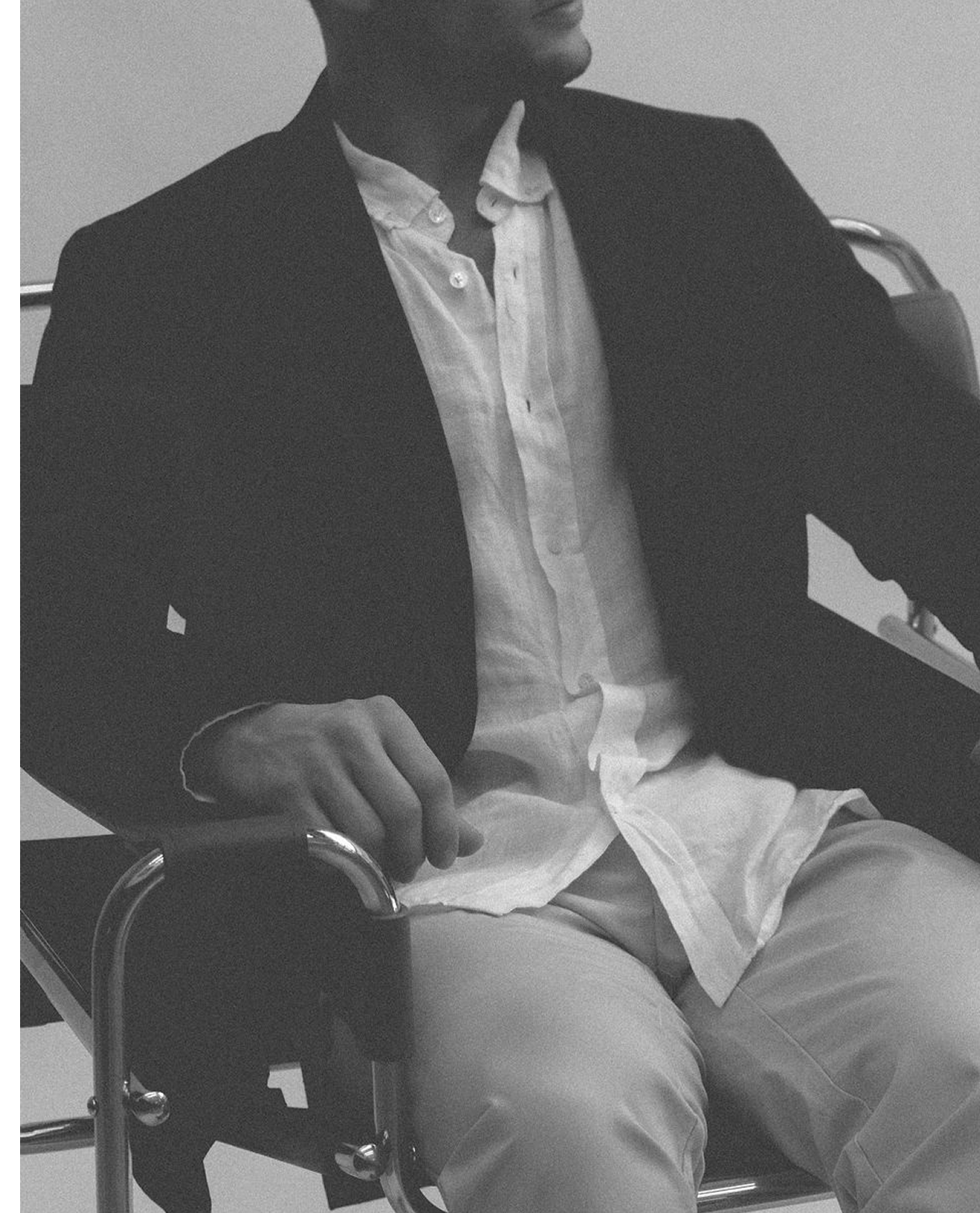 Man seated, adjusting his jacket, in black and white