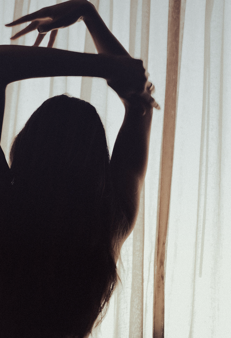 Woman with arms raised, hair falling, backlit by window light