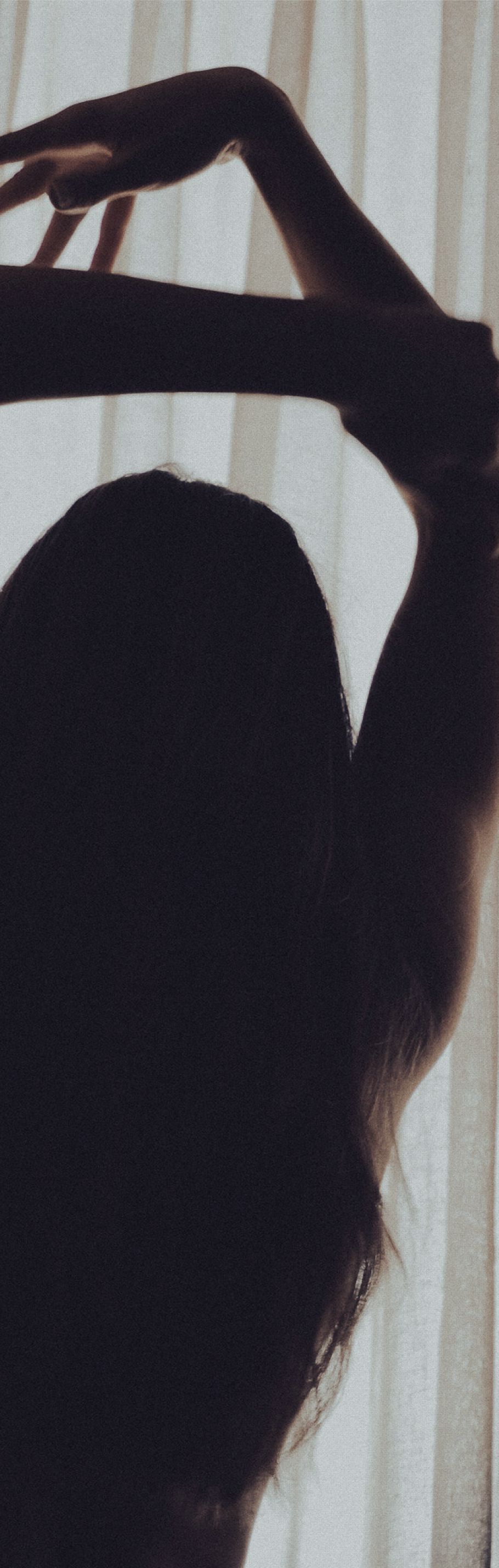 Woman with arms raised, hair falling, backlit by window light
