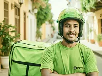 Smiling delivery man in green uniform and helmet carrying a green insulated backpack outdoors.