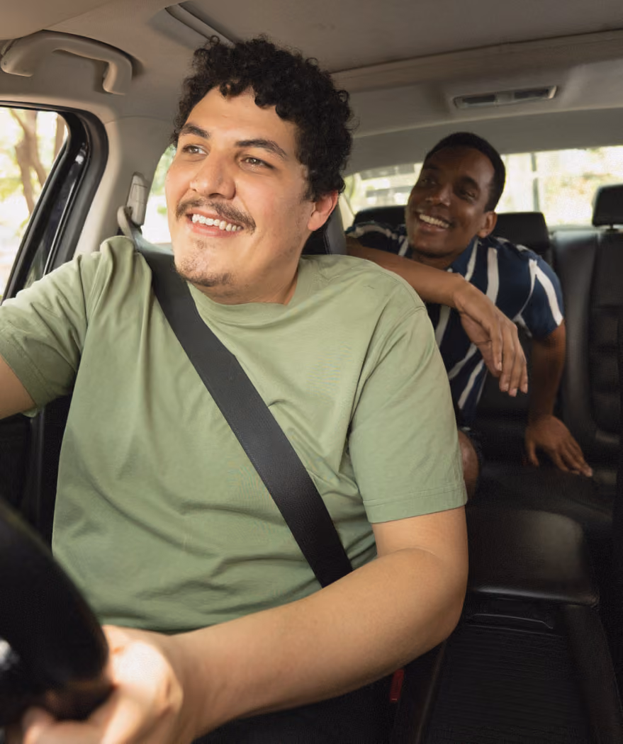 Man in a green shirt driving a car with a smiling passenger in a blue striped shirt behind him.