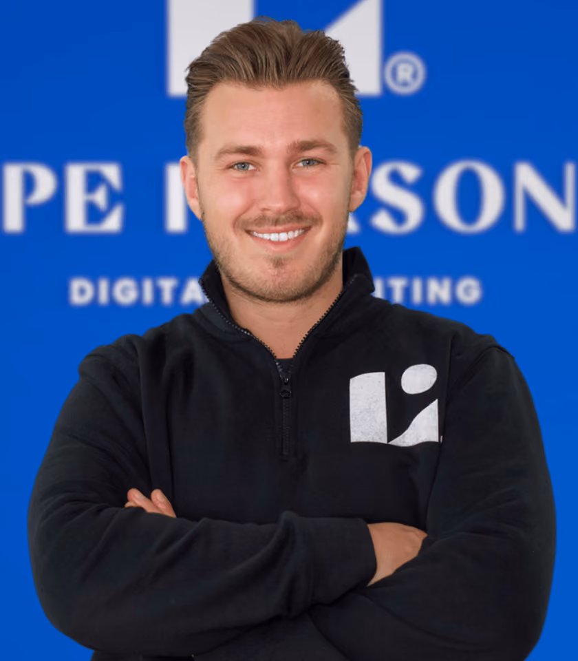 Lächelnder Mann mit schwarzem Pullover vor blauem Hintergrund mit Logo.