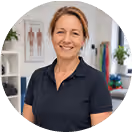 Freundliche Frau in einem Fitnessstudio, Skelett-Poster im Hintergrund, Hanteln und Fitnessbänder.