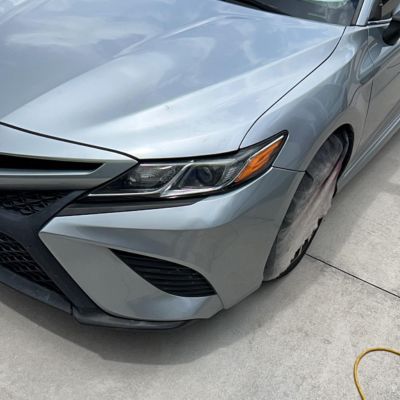 Close-up of a silver car's front bumper and headlight after bumper repair on a concrete surface.
