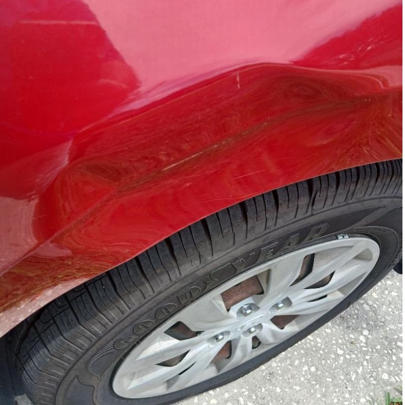 Red car fender with a dent above a Goodyear tire and silver alloy wheel.