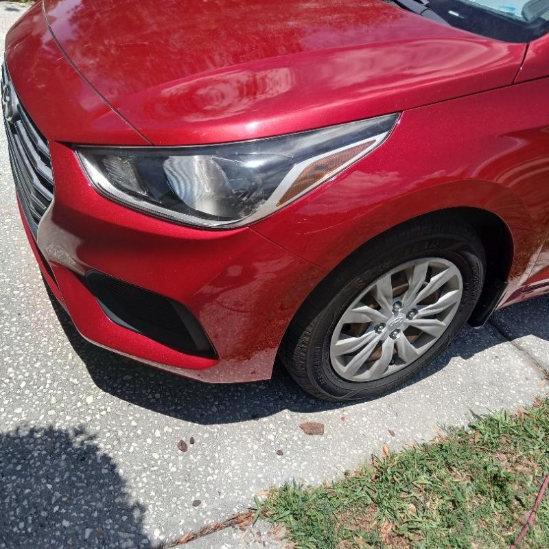 Red car front left side showing headlight, wheel, and fender with a small dent visible on the fender.