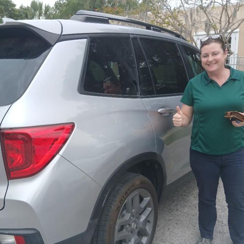 Smiling woman in green shirt giving thumbs up next to a silver SUV Before and after mobile bumper scrape repair by Paint N Go