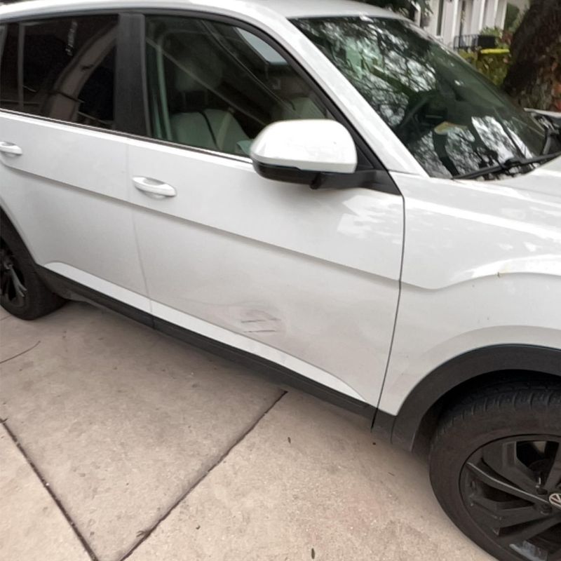 White car with a dent and scratch on the passenger front door panel parked on concrete driveway.