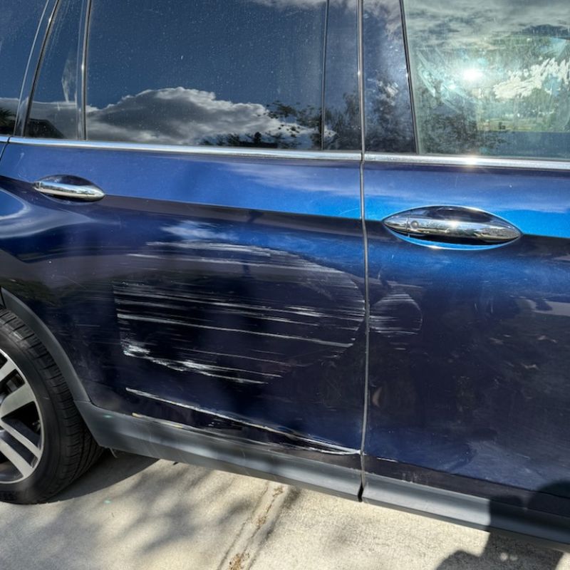 Blue Honda Pilot with heavy scrape damage across the passenger-side rear door in Tampa