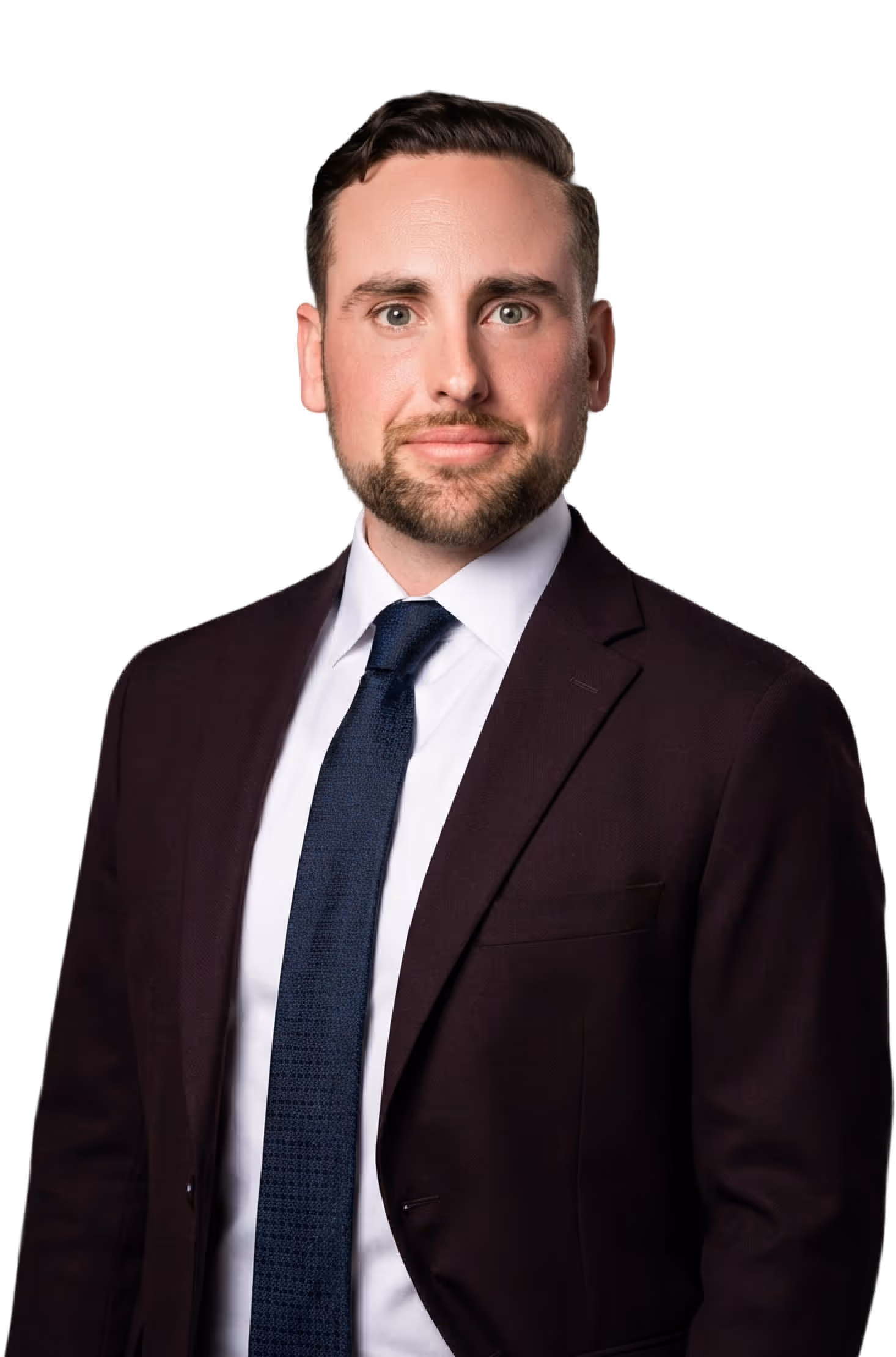 Portrait of a man with short dark hair and beard wearing a dark suit, white shirt, and blue tie against a black background.