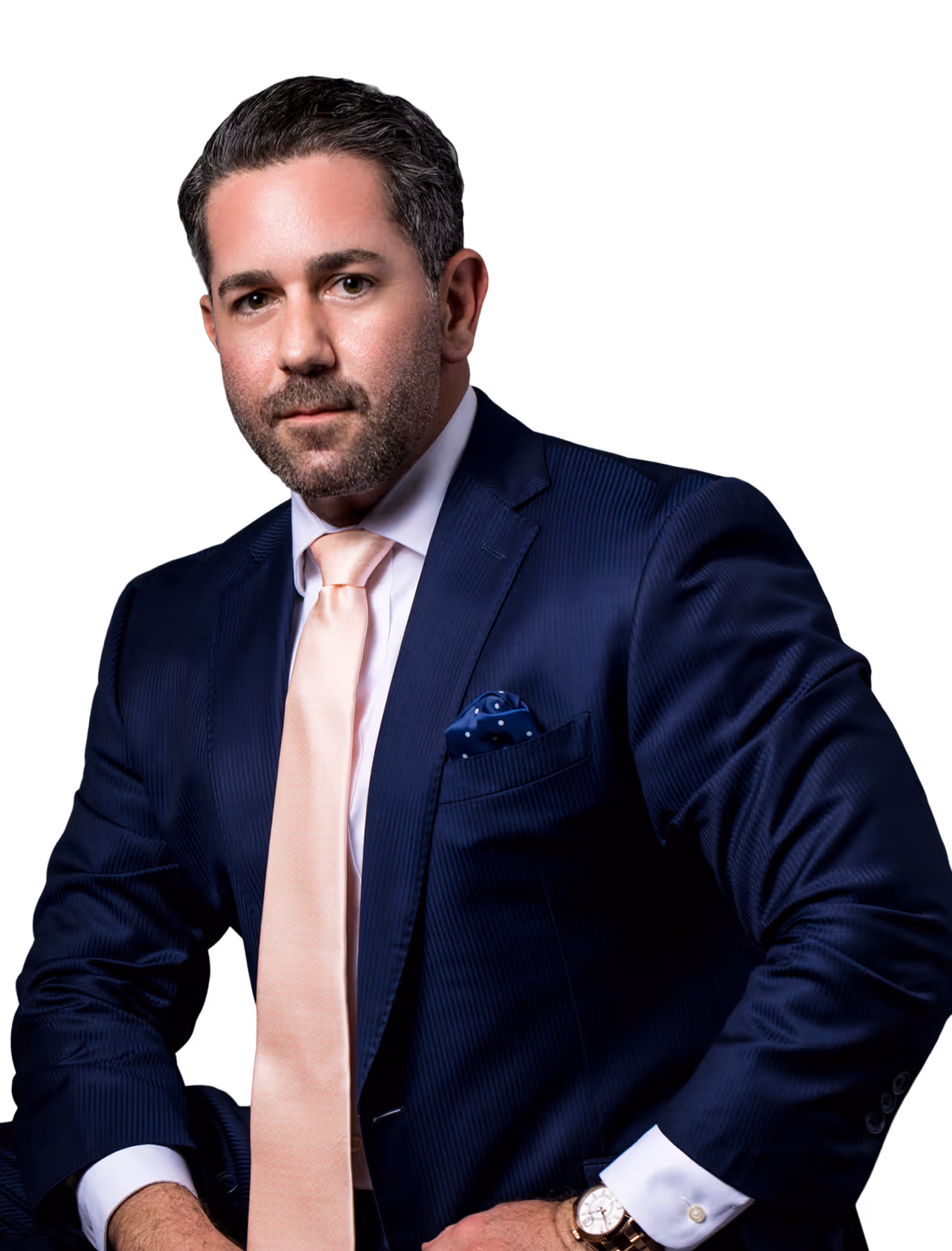 Portrait of a man in a navy blue suit with a light pink tie and a blue polka dot pocket square, posing against a black background.