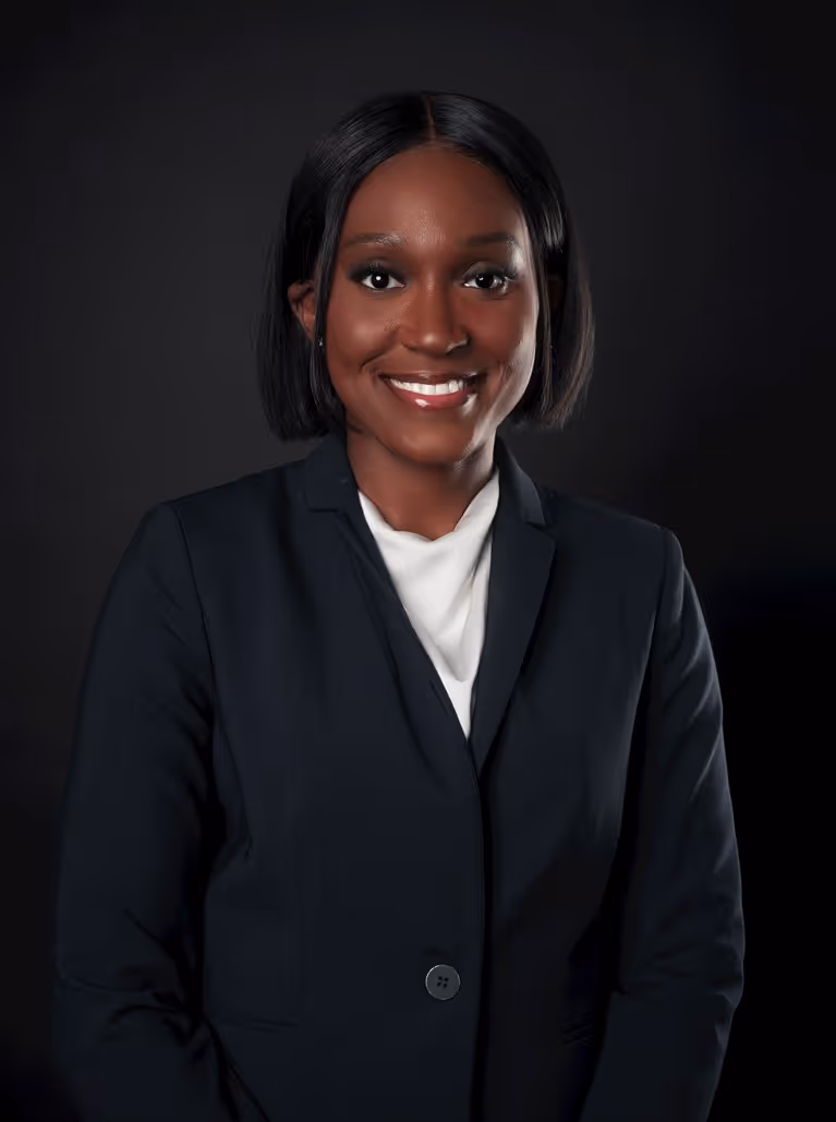Smiling professional woman with short black hair wearing a dark blazer and white shirt, posing against a black background.