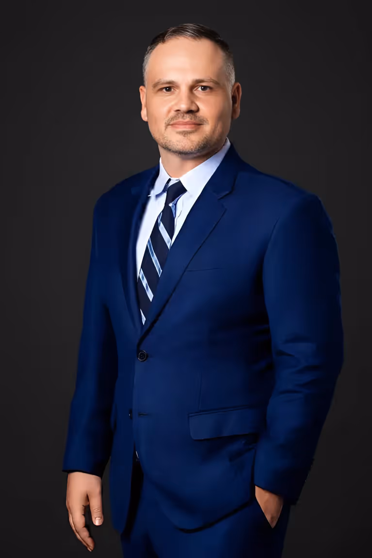 Man in a blue suit and striped tie standing against a dark background.