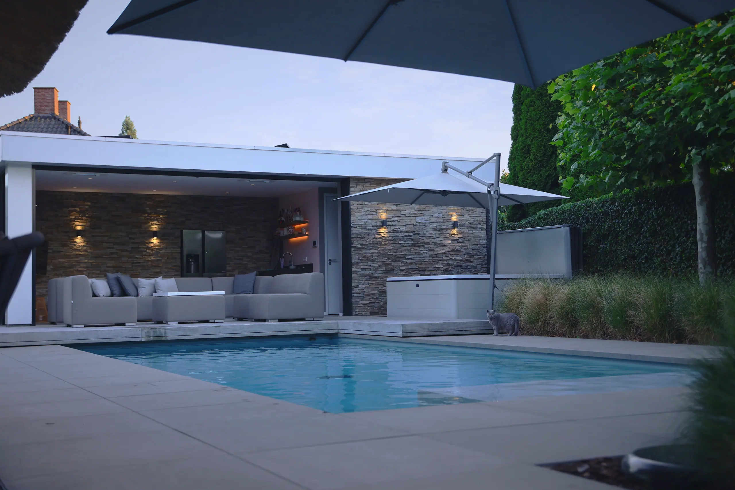 Zwembad met poolhouse, loungeset en parasols in de avondschemering.