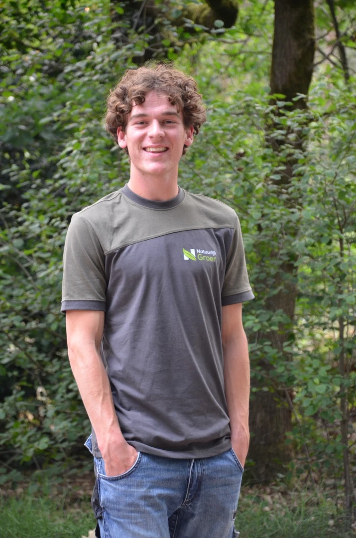 Medewerker van Natuurlijk Groen in bedrijfsshirt tussen het groen.