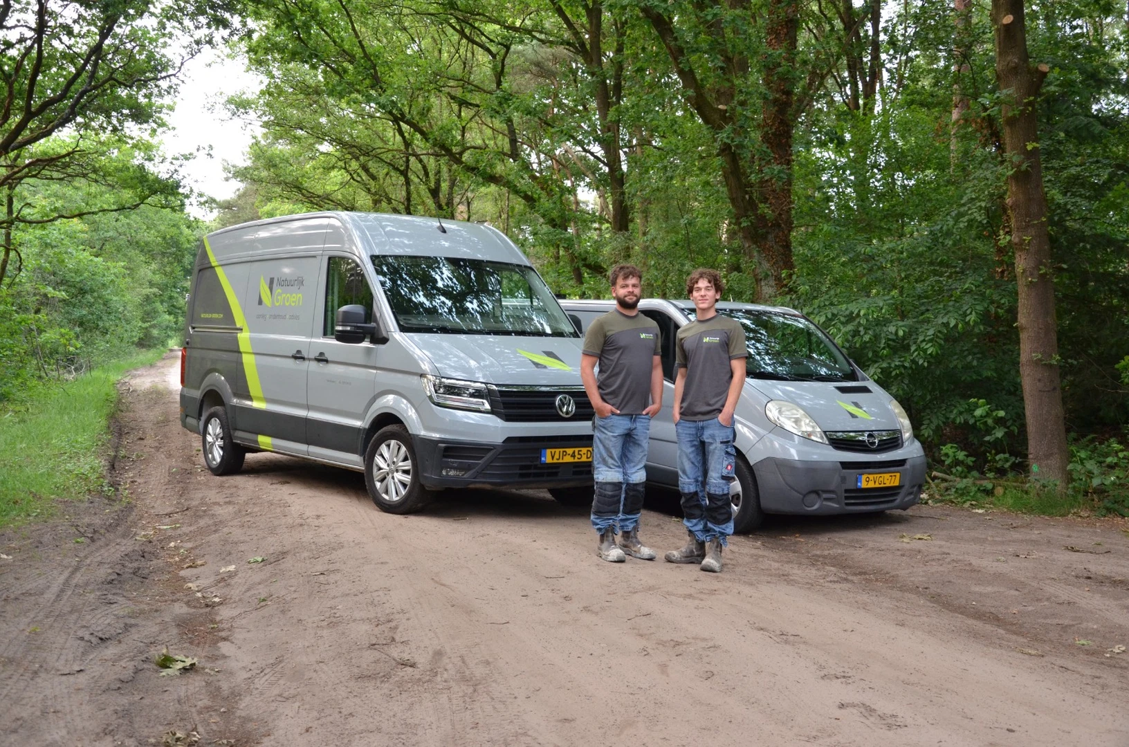 Twee hoveniers van Natuurlijk Groen bij de bedrijfsbussen op een bospad.