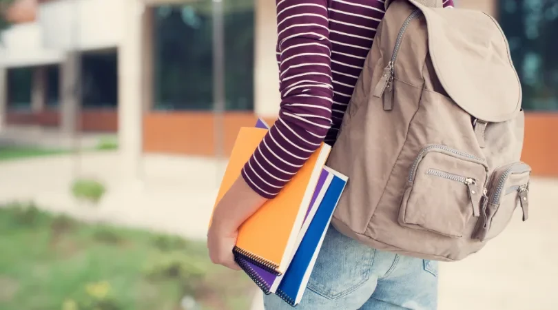 A person with a bacpack holding books
