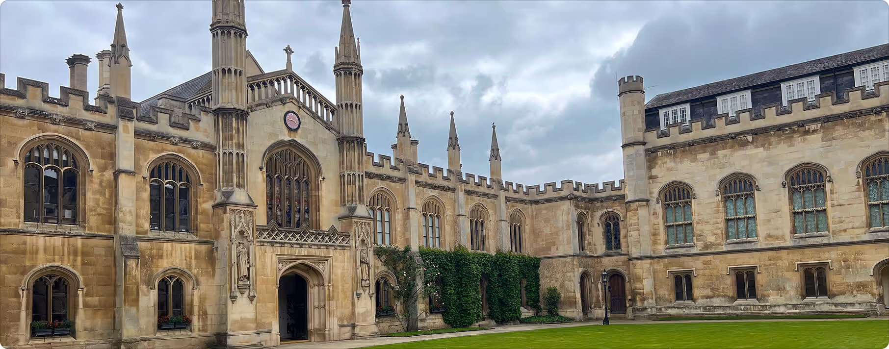 Historic stone building with Gothic architecture, pointed spires, stained glass windows, and a green ivy-covered wall, under a cloudy sky.