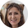 Smiling woman with styled hair and natural makeup against a blurred background.