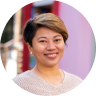 Smiling Asian woman with short hair wearing a purple top in an outdoor setting.