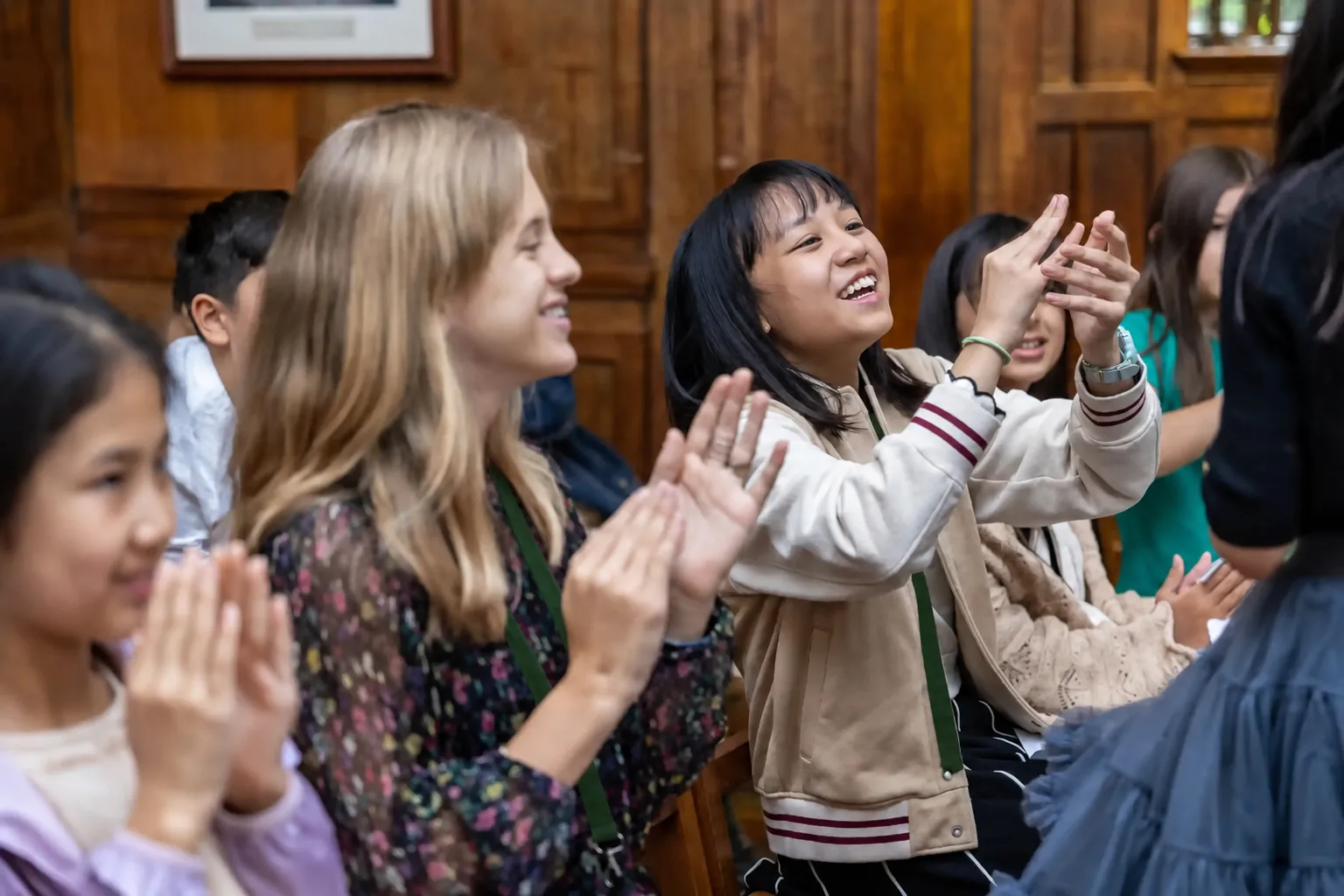 A group of diverse students clapping and smiling enthusiastically in a classroom setting.