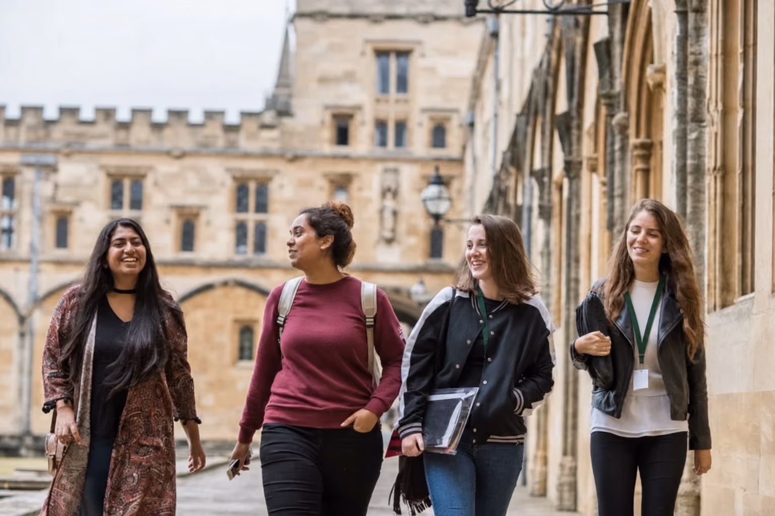 Four students walking and talking together through a college quad in Oxford