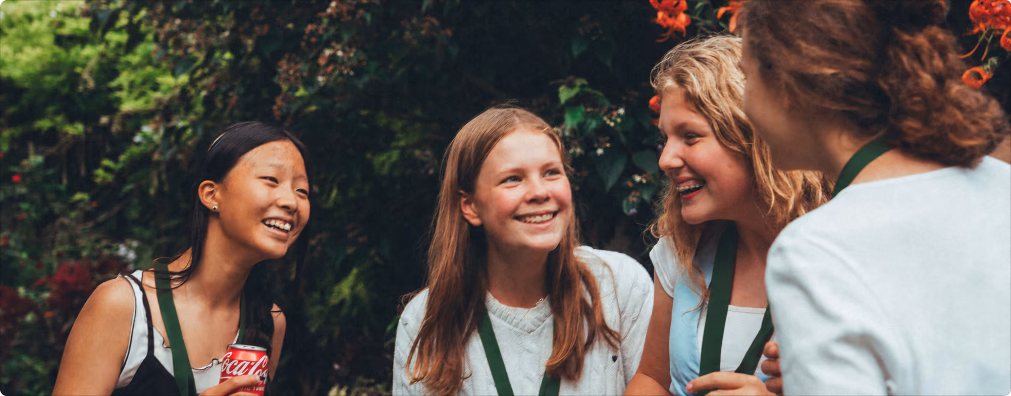 Younger students in green lanyards laughing together outdoors in a garden