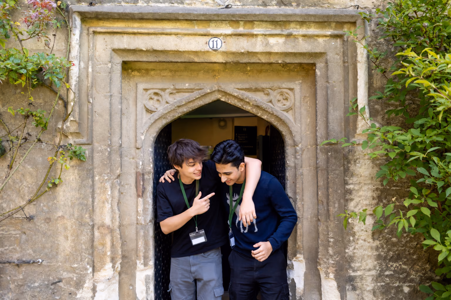 Two students laughing in the arched stone doorway of a college building