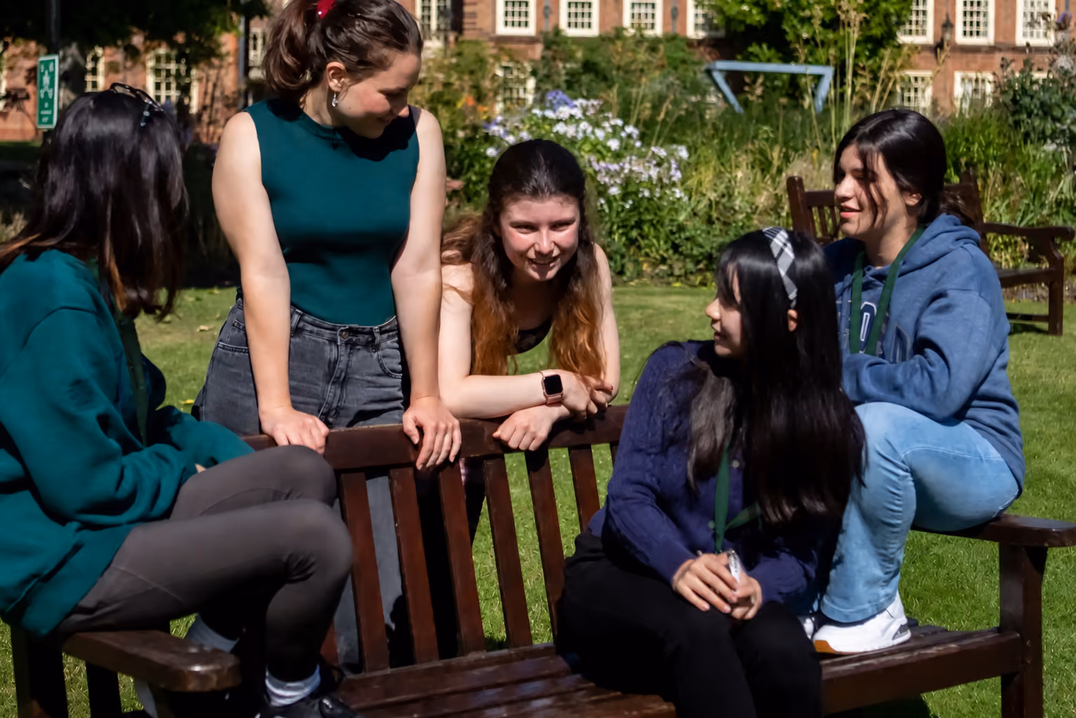 Students chatting around a wooden bench in a sunny college garden