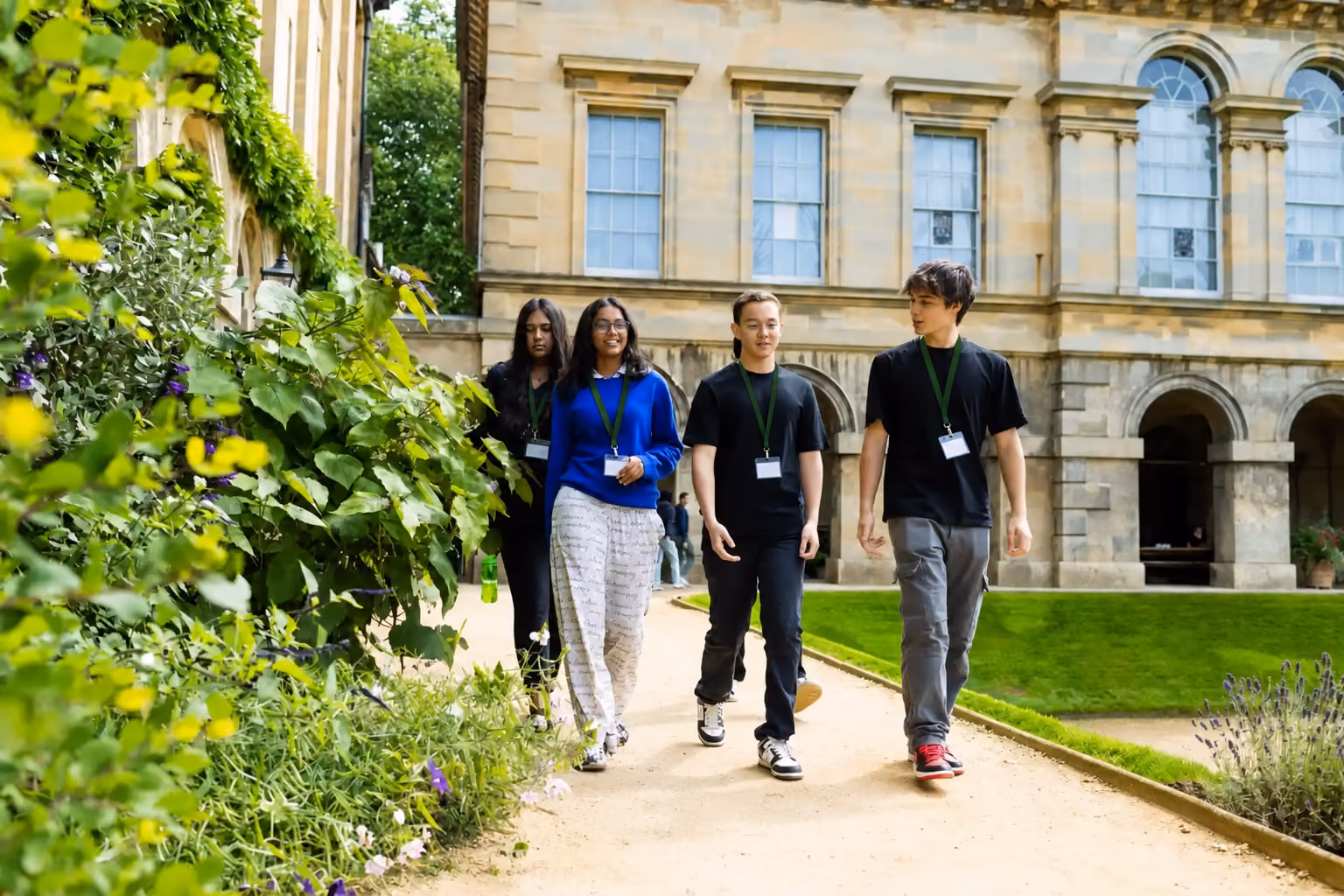 Four students walking along a garden path beside a college building in Oxford