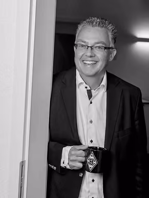 Fröhlicher Mann im Anzug mit Brille hält eine Borussia Mönchengladbach Tasse.